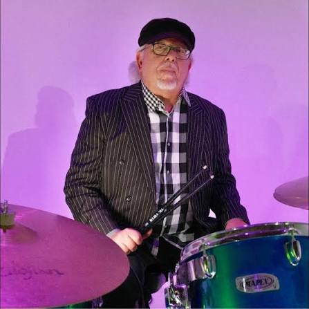 John Borack seated behind a drum kit under purple stage lighting
